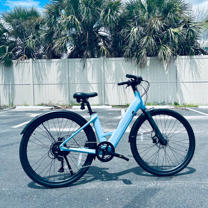 Urtopia Carbon ST Glacier Blue ebike parked outside empty parking lot with palm trees behind it. 