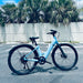 Urtopia Carbon ST Glacier Blue ebike parked outside empty parking lot with palm trees behind it. 