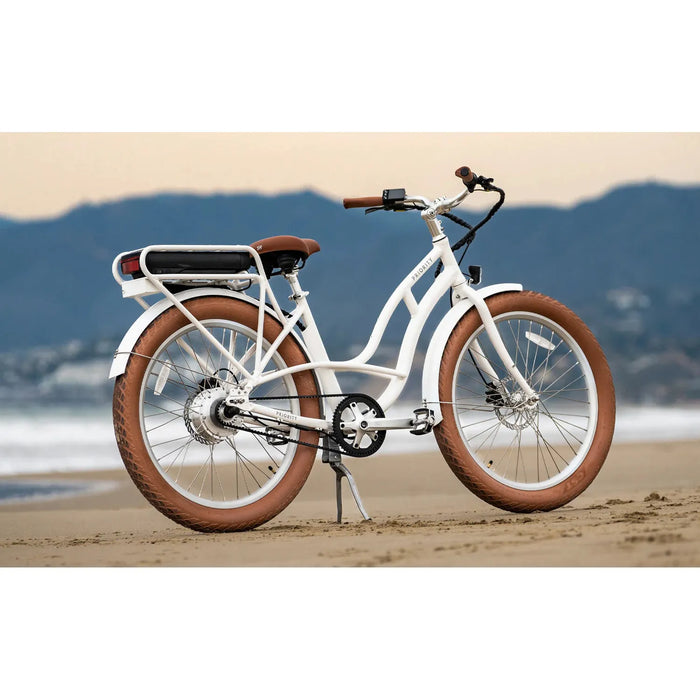 White Priority E-Coast ebike parked on the beach with mountains in the background.