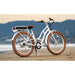 White Priority E-Coast ebike parked on the beach with mountains in the background.